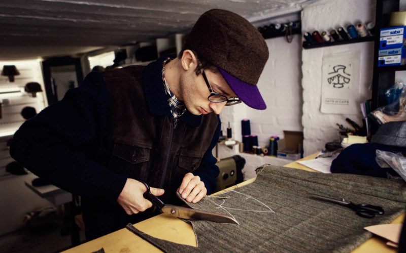 The capmaker Silas Gärtner cutting fabric with a scissor