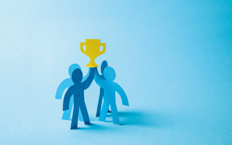Four blue people made from cardboard holding award on blue background